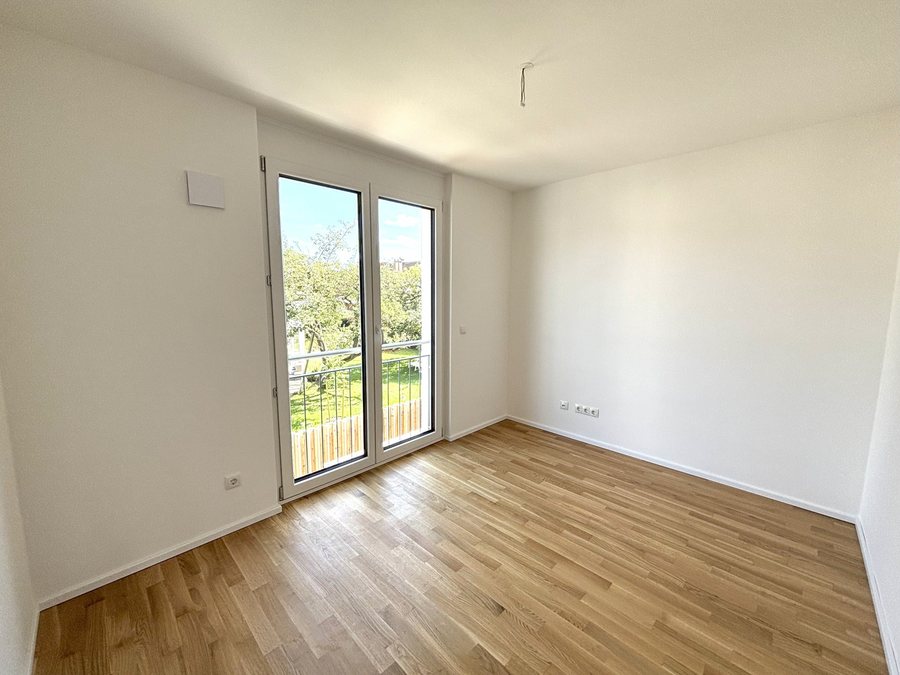Zimmer mit Eichenparkett und bodentiefer Fenstertür mit Blick ins Grüne